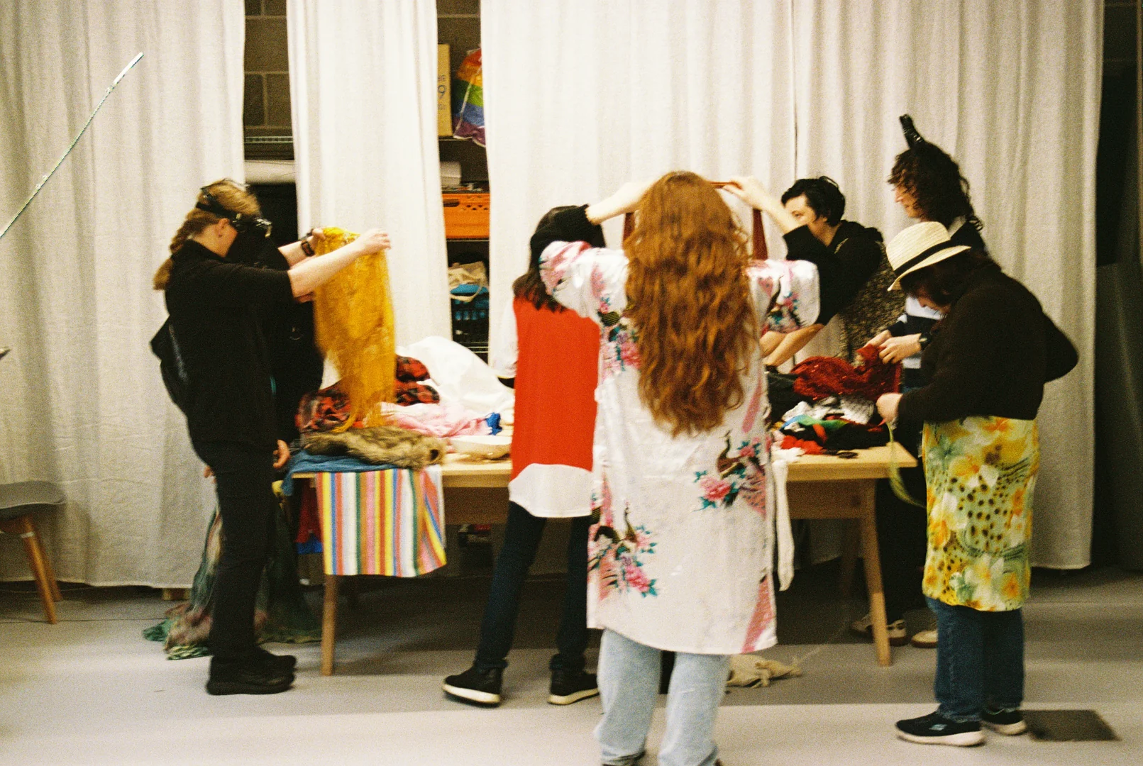 Workshop participants gather around a table of clothes and fabrics as they prepare outfits.